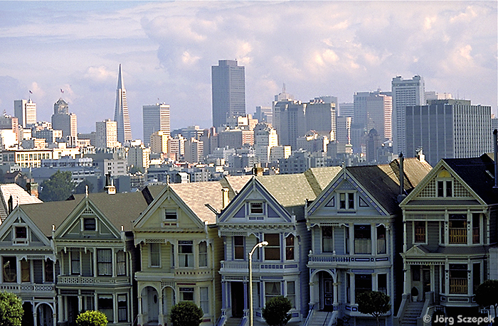 Blick über den Alamo Square Park auf die pittureske Häuserzeile der Postcard Row vor der modernenen Kulisse San Franciscos´